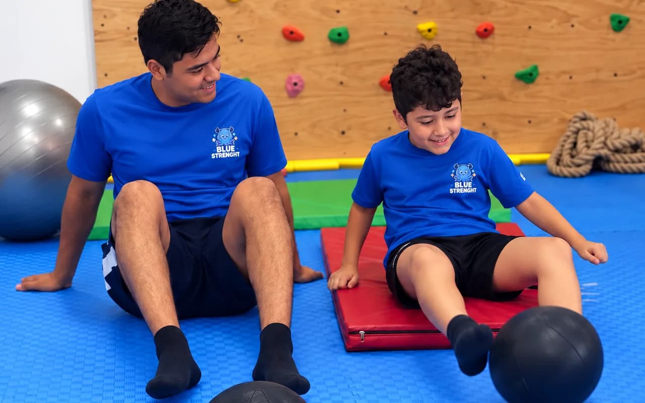 Un niño y un joven, sentados sobre tapetes, empujan balones con los pies.